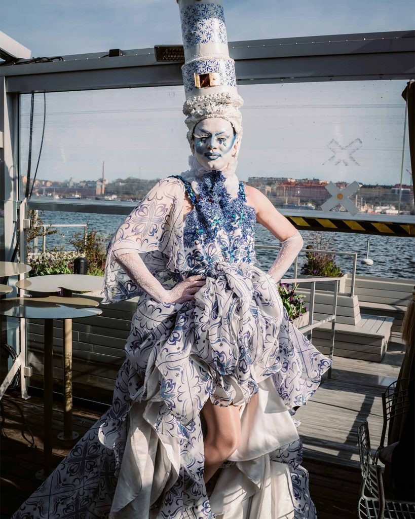 A drag queen poses on the waterfront in an elaborate outfit. 