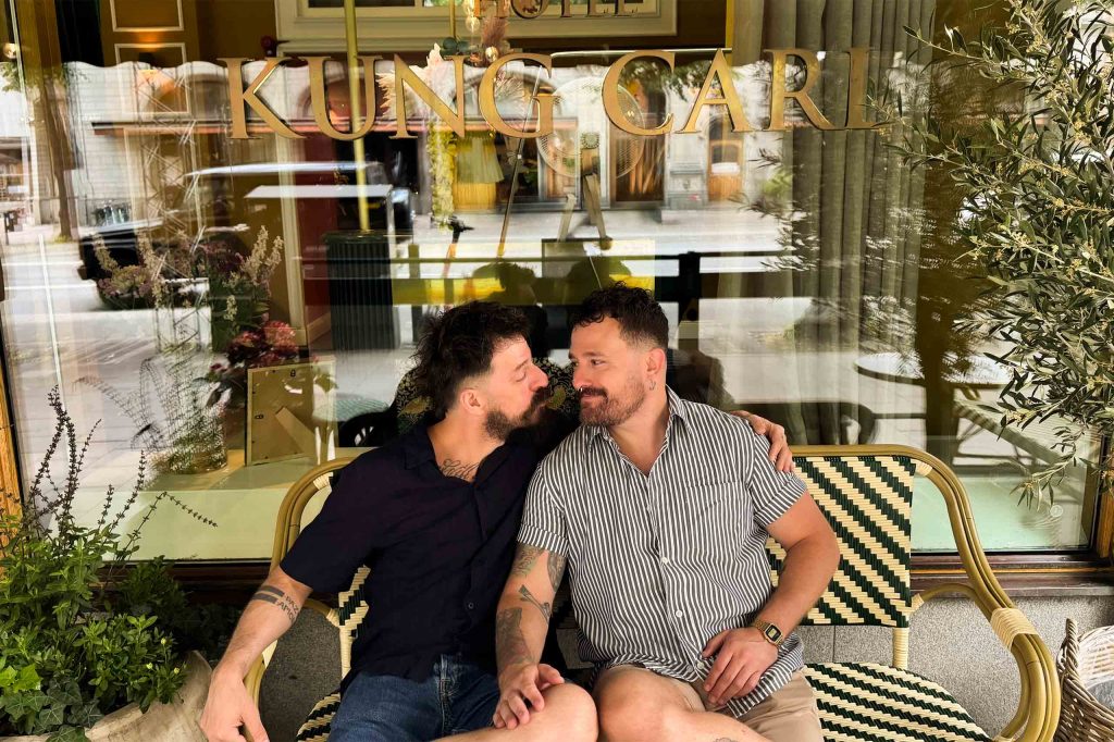 A gay couple hugging at an outdoor seating area.