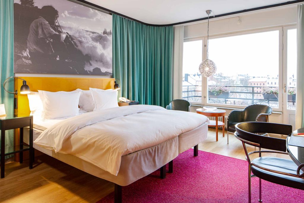 De luxe hotel room with a private balcony at Hotel Rival, an LGBTQ+ welcoming boutique hotel in Stockholm, with artwork above the bed and views over Södermalm rooftops