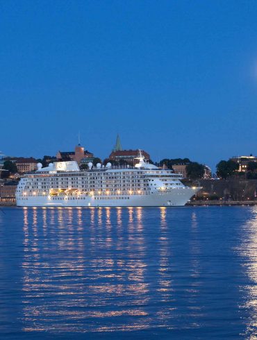 Cruise ship in Stockholm harbour, next to large sail boat in the late evening with a full moon in the sky reflected in the water