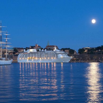 Cruise ship in Stockholm harbour, next to large sail boat in the late evening with a full moon in the sky reflected in the water