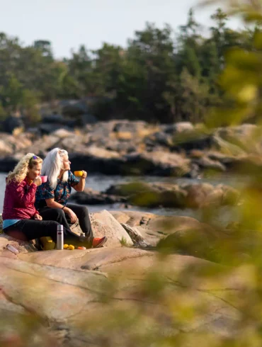 A lesbian couple sit on rocks near the waterfront in a rural part of Stockholm.