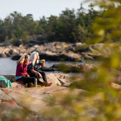 A lesbian couple sit on rocks near the waterfront in a rural part of Stockholm.