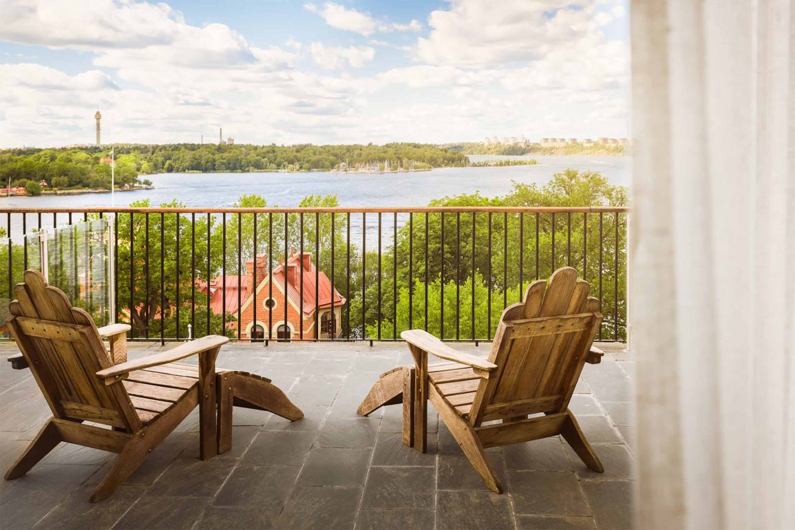 Two wooden chairs on a terrace at Hotel J, overlooking a calm waterway.