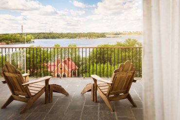 Two wooden chairs on a terrace at Hotel J, overlooking a calm waterway.