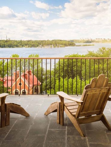 Two wooden chairs on a terrace at Hotel J, overlooking a calm waterway.