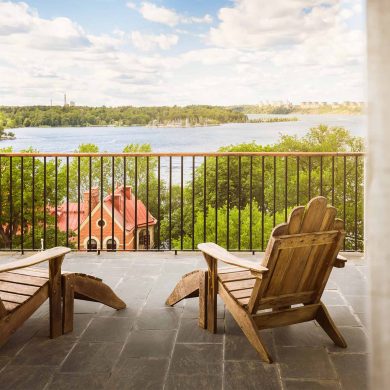 Two wooden chairs on a terrace at Hotel J, overlooking a calm waterway.