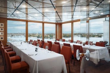 A private dining room with sprawling views of Stockholm. The chairs are red, and the tablecloths are white.
