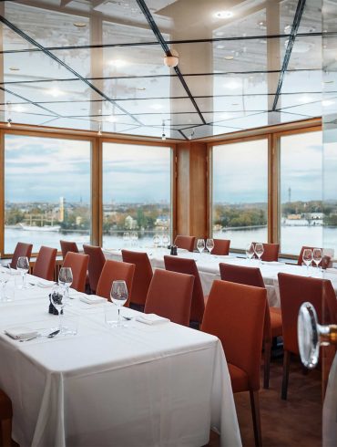 A private dining room with sprawling views of Stockholm. The chairs are red, and the tablecloths are white.