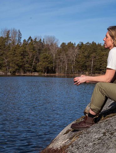 A woman sits on a rock overlooking a lake. The lake is surrounded by a forest.